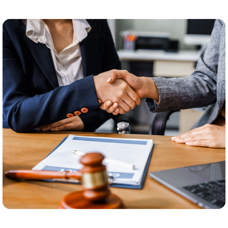 Two female lawyers in business suits shake hands at wooden desk, finalizing legal agreement.